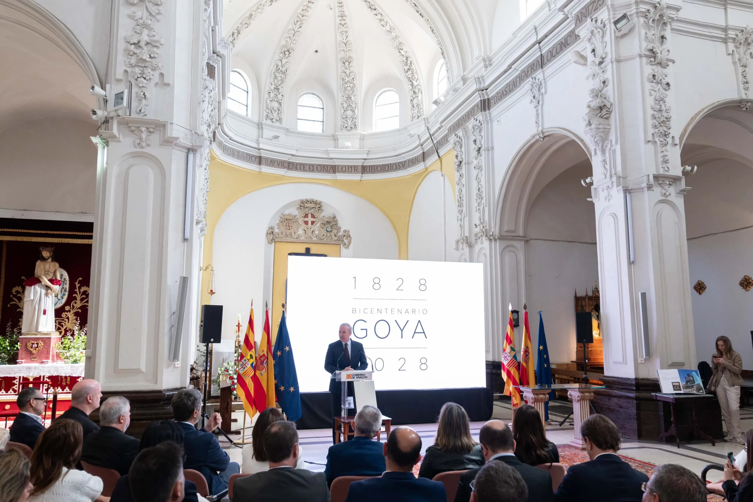 Presentación del Plan del Bicentenario de Goya en Aragón. Acto institucional en una iglesia durante la presentación del plan del Bicentenario de Goya, con un orador en el atril y público asistente.