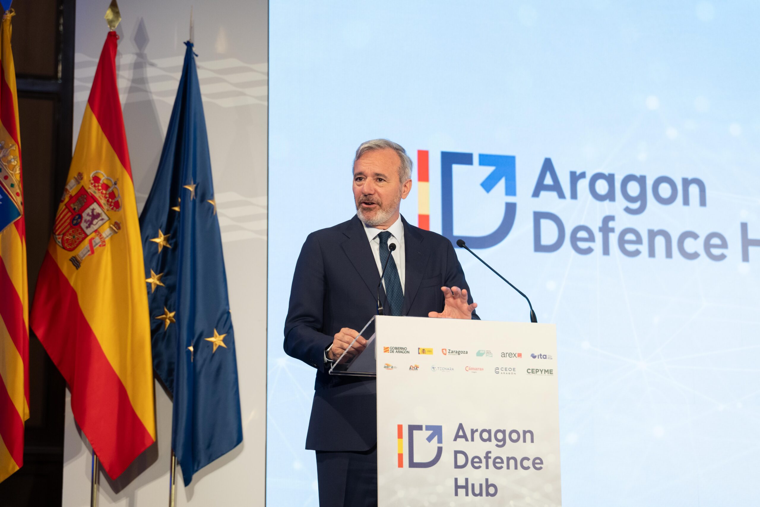 Presentación del Hub de Defensa de Aragón El presidente de Aragón presenta el Hub de Defensa de Aragón durante un acto institucional acompañado de banderas oficiales