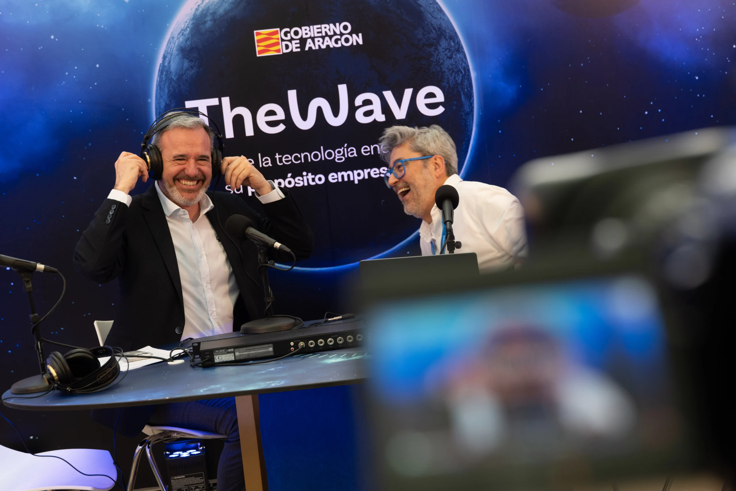 Grabación en el congreso tecnológico The Wave, con dos ponentes en un set de radio y micrófonos ante el fondo del evento
