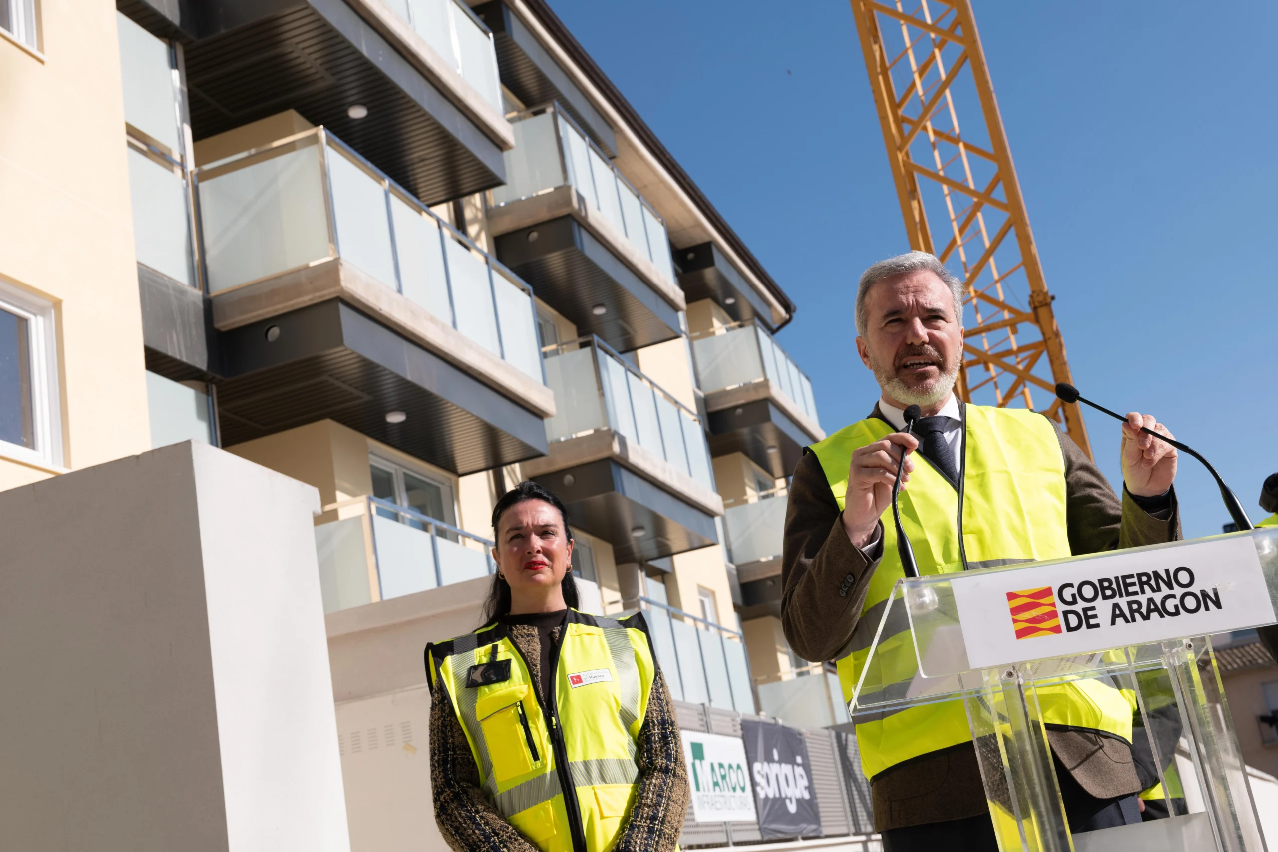 Visita institucional a una promoción de vivienda pública en Huesca, con edificio en construcción y grúa